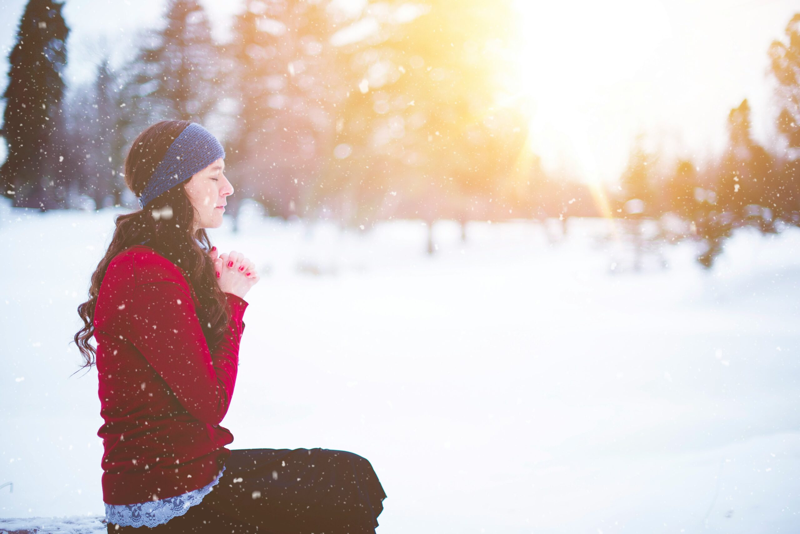 A woman meditates in the snow as the sun sets